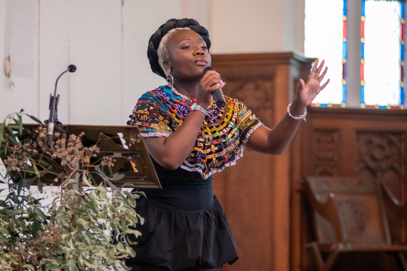 Marie-Paul speaking into a microphone in a colorful top